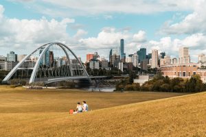Two girls are seen sitting on Walterale hill overlooking the Walterdale Bridge in the summer time.