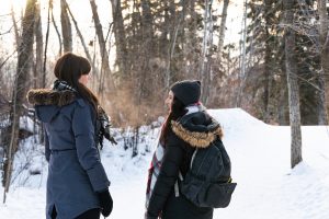 Two women walk in the snow-covered river valley during winter.