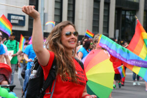 A woman in a red t-shirt waves a rainbow flag at PrideFest.