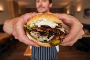 Hands holding up a burger from Fox Burger close to the camera.