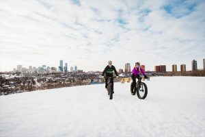 man and woman fat bike on a hill over looking Edmonton's downtown skyline