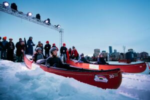 A group get ready to race down a snowy hill in red canoes at the Flying Canoe Volant festival.