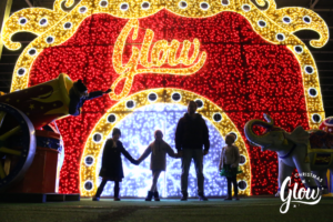 The silhouette of a family standing in front of a wall lit with lights that say "Glow".