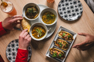 Hands reaching for dishes on a table by Sauce Modern Carribbean Cuisine.