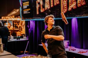 A man tosses a cocktail shaker into the air while making a drink.