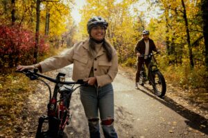 A woman and a man smile as they ride their bikes in the fall.