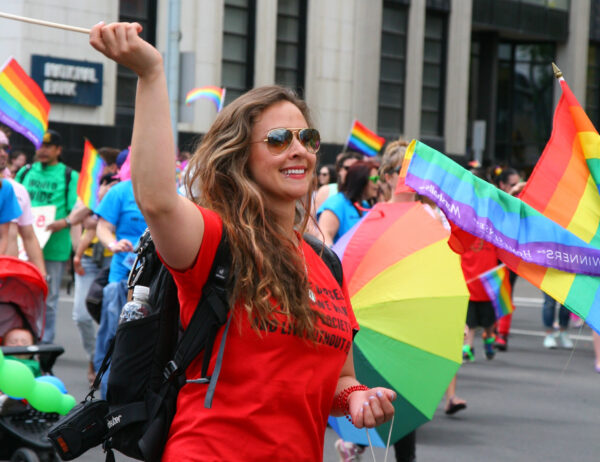 A woman in a red t-shirt waves a rainbow flag at PrideFest.