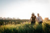 A couple walks through Edmonton's river valley with the city skyline behind them.