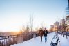 A couple, holding hands, walk along Edmonton's Victoria Promenade at sunset. It's the winter season. They each have a coffee in hand and a smile on as they admire the view of the river valley