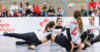 Four women volleyball players from Canada's Sitting Volleyball team are seen playing a game of volleyball at Edmonton EXPO Centre. One woman is seen diving to bump the ball that's in mid air while the other three players watch and move back to make room for her to hit the ball.