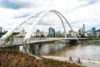 A couple is riding bikes in the North Saskatchewan River Valley near the Walterdale Bridge with the skyline in the background.