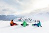 a group of snowboarders sit at the top of a ski run