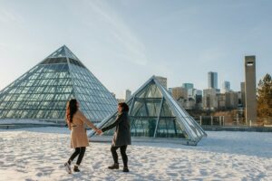 Two people hold hands in front of the Muttart Conservatory.