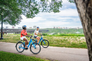 Tour Two people cycle on a path at Ezio Faraone park with the river valley in the background.