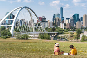 A couple sits in the river valley at Walterdale Hill, looking at the downtown skyline.