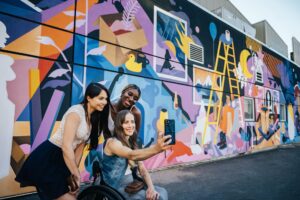 Three people pose for a selfie in front of a mural.