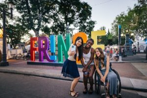 Three people take a selfie in front of Edmonton's Fringe Festival sign.
