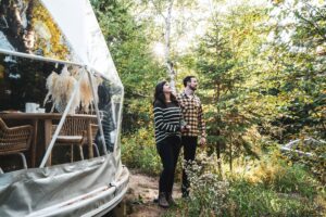 A couple camping in nature outside of a geodesic dome.