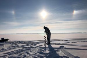 A man drills a hole in the ice in preparation to fish.