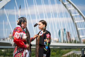 A mother and daughter in traditional Indigenous clothing in front of the Walterdale Bridge