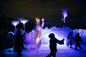 A group of performers walk down an icy path while holding light sticks at night