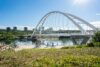 People bike by a large bridge and river