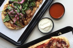 Two pizzas and two sauces sitting on a table.