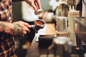 Tattooed man tamping coffee